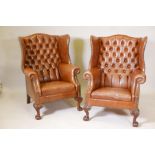 A pair of button back brown leather wing armchairs, on carved ball and claw feet, 41" high