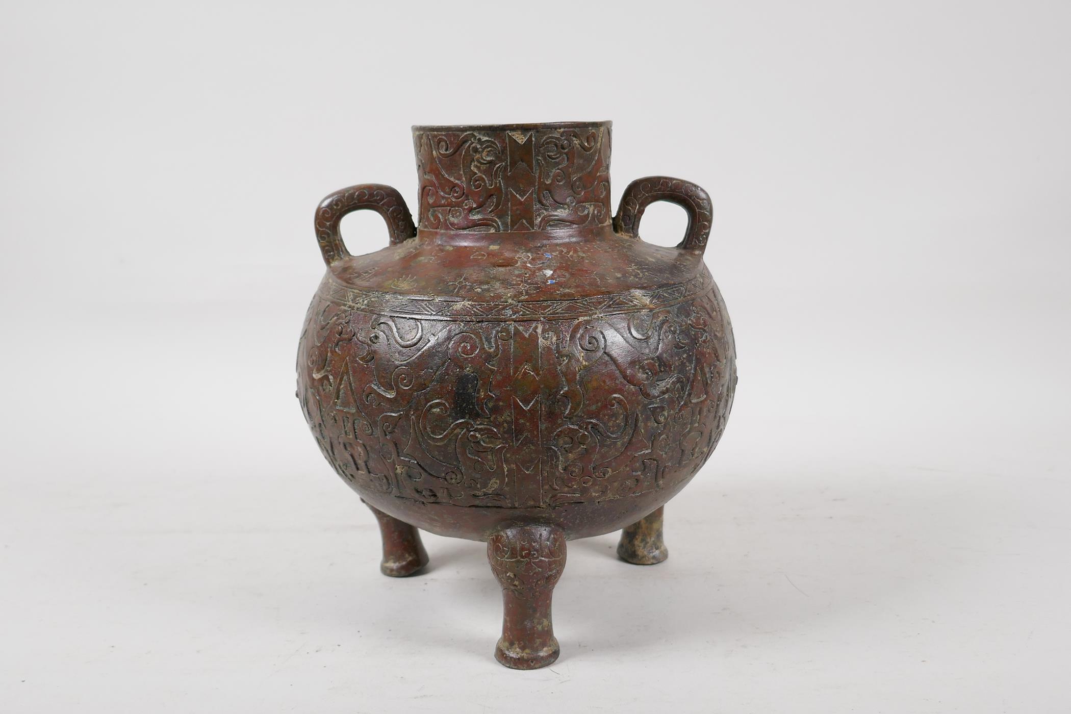 A Chinese bronze two handled vase raised on tripod supports, with raised and engraved archaic