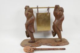 An oriental carved wood table gong supported by two dressed monkeys, 11" high, 15" wide