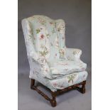 A 1930s oak high back wing armchair, raised on turned supports