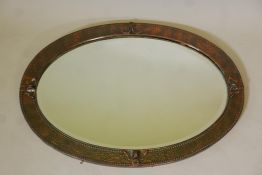 An Arts & Crafts hammered copper wall mirror with decorative mounts and bevelled glass, 35" x 24"