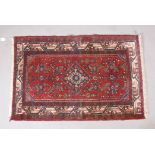 A Persian red ground wool rug with a central medallion design and cream borders, 46" x 30"
