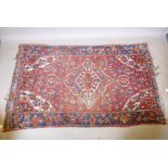 A Persian red ground wool carpet with a central floral medallion design and blue borders, 83" x 52"