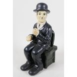 A ceramic figurine of Charlie Chaplin seated in a chair, 10" high