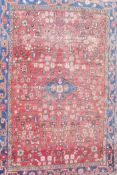 A Persian hand woven full pile rug with an all over floral design on a red field, with blue