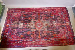 A Persian Hamadan deep pile worn wool red ground rug, decorated with a floral and geometric