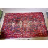 A Persian Hamadan deep pile worn wool red ground rug, decorated with a floral and geometric