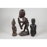 An African carved hardwood figure carrying a rain stick, with white painted details, and two other