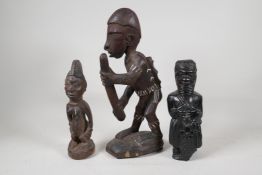 An African carved hardwood figure carrying a rain stick, with white painted details, and two other