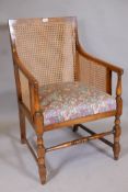 A 1930s bergere arm chair with cane back and sides and drop in seat, raised on turned supports