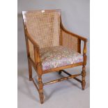 A 1930s bergere arm chair with cane back and sides and drop in seat, raised on turned supports