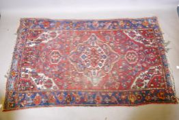 A Persian red ground wool carpet with a central floral medallion design and blue borders, 83" x 52"