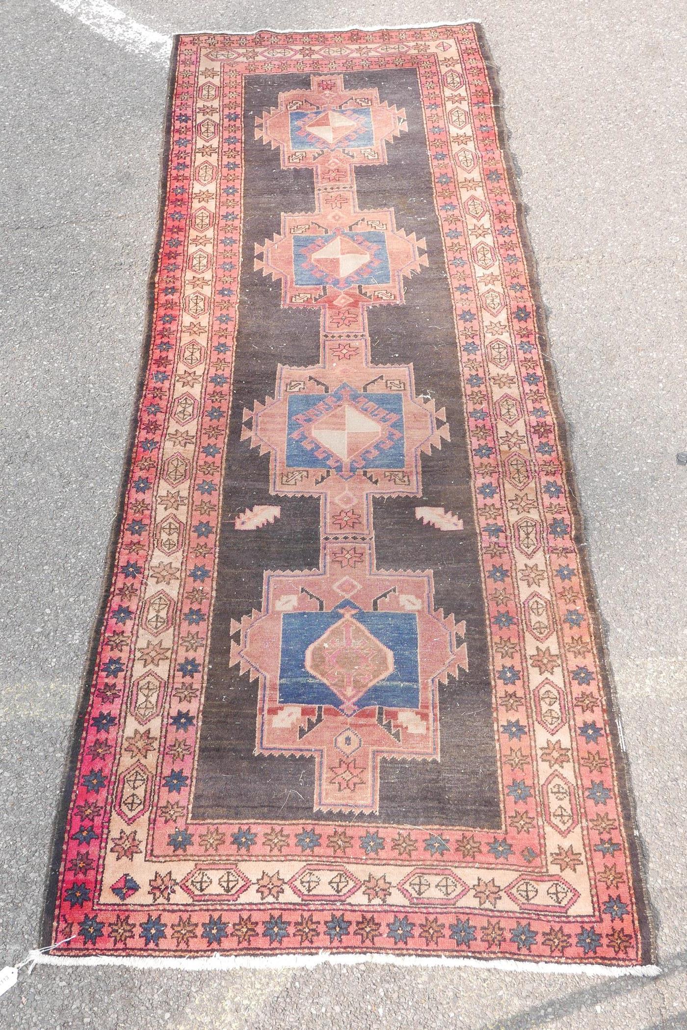 A Persian black ground hand woven wool runner with a repeating rust coloured medallion design within - Image 2 of 6