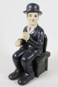 A ceramic figurine of Charlie Chaplin seated in a chair, 10" high