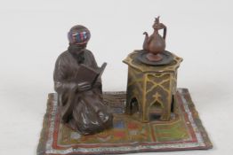 A gold painted bronze inkwell, modelled as an Arab gentleman reading, beside a table that forms