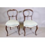 A pair of Victorian walnut balloon back side chairs, with carved and pierced back rails, raised on