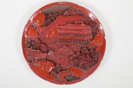 A Chinese cinnabar lacquer style dish, with carved decoration of temples in a riverside landscape,