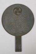 A Japanese bronze hand mirror, decorated with the Mitsudomoe, a fruit bearing bush, and character