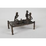 An African benin bronze of figures sharing a meal, on a raised bed, 6" x 3½"
