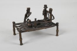 An African benin bronze of figures sharing a meal, on a raised bed, 6" x 3½"