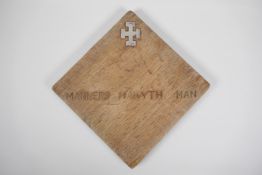 An oak panel with inset hallmarked silver cross potent and the inscription, "Manners Makyth Man".