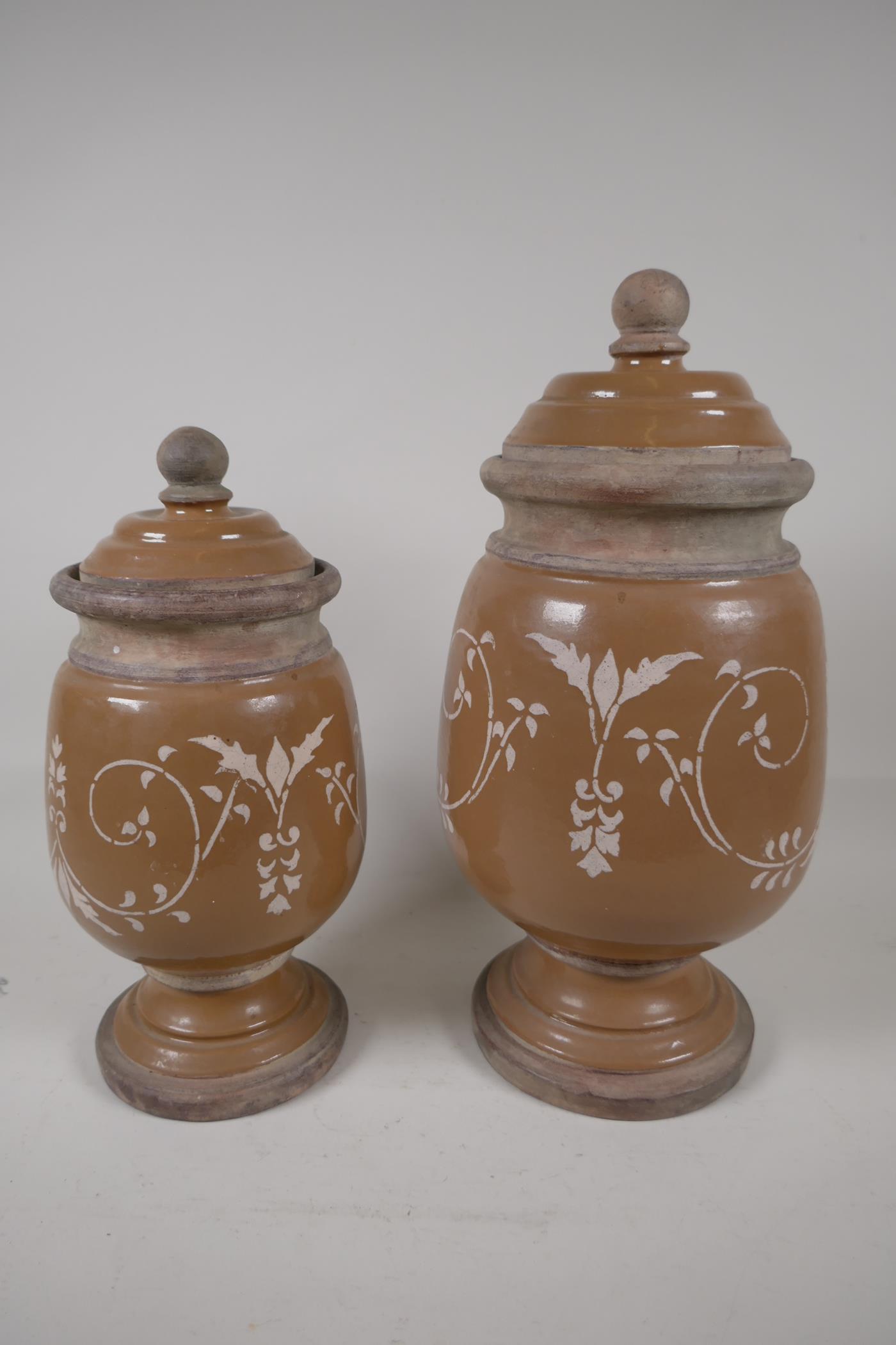 Two French stoneware lidded storage jars on pedestal bases, having painted scrool decoration.
