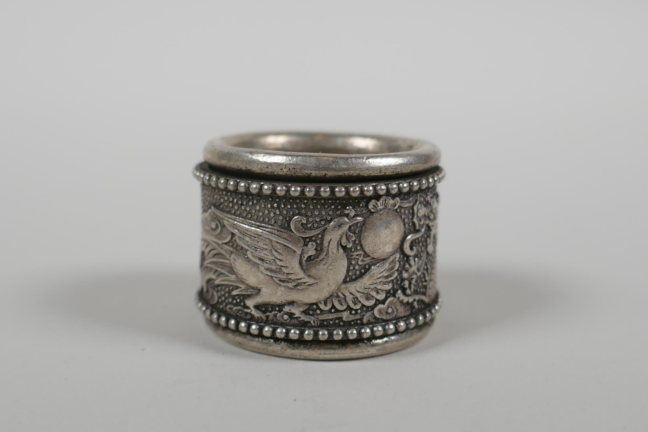 A Chinese white metal archers thumb ring with a revolving cuff decorated with a dragon and