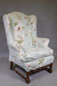 A 1930s oak high back wing armchair, raised on turned supports