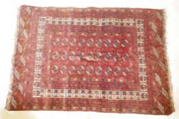 A vintage Bokhara hand woven wool carpet with central geometric pattern on a red field with white