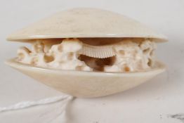 A Japanese netsuke in the form of a clam shell, carved with a mountain scene, signed, 2" long