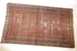 an antique hand woven Persian carpet with geometric designs on a red field with blue borders, 46"