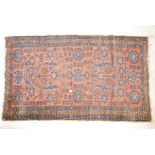An antique, hand woven wool carpet. With blue geometric designs and floral motifs, on a terracotta