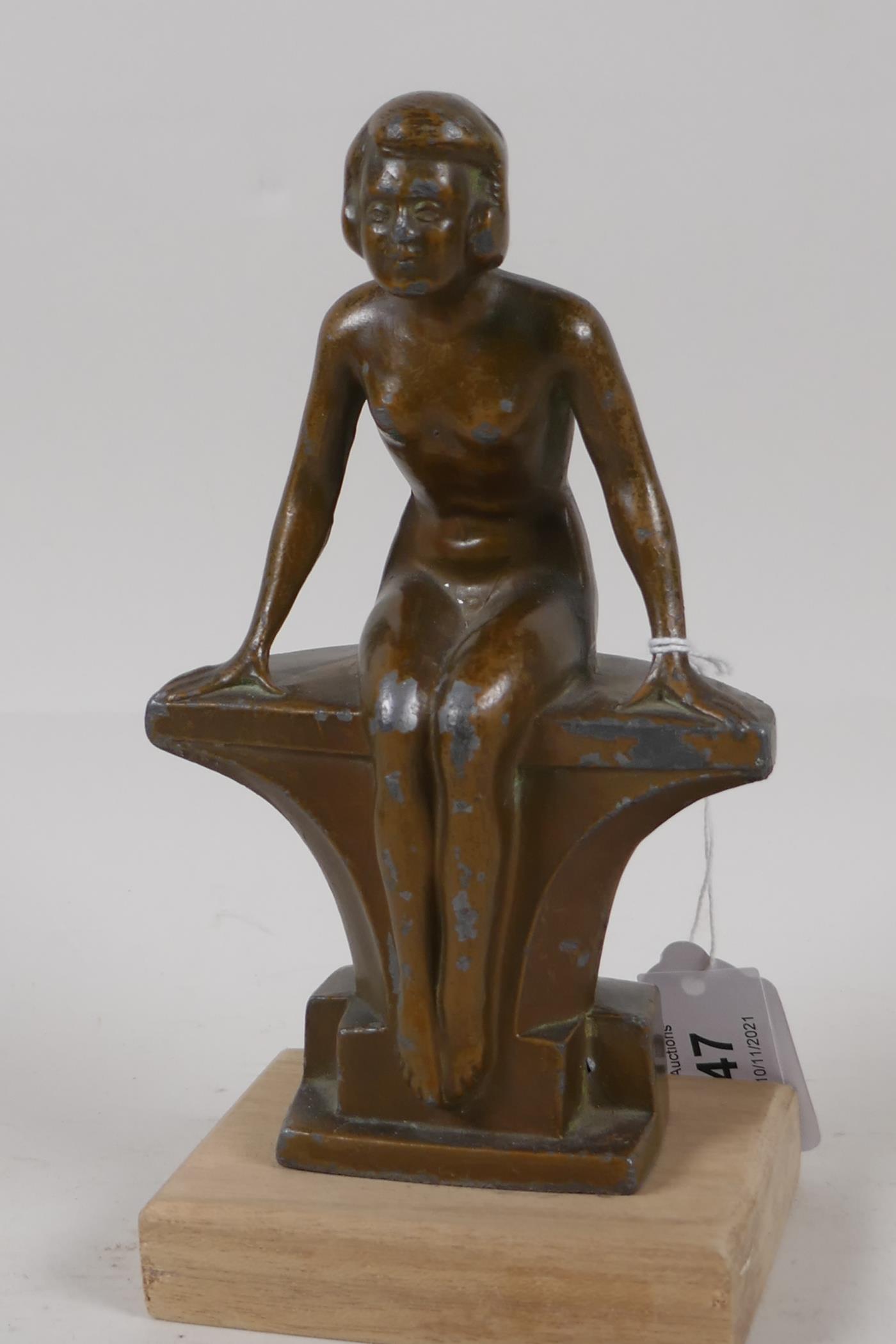 An Art Deco bronzed spelter figurine of a nude girl seated on a bench, 7½" high