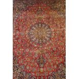 A large red ground Persian Mashhad carpet with a multicolour traditional floral medallion design,