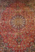 A large red ground Persian Mashhad carpet with a multicolour traditional floral medallion design,