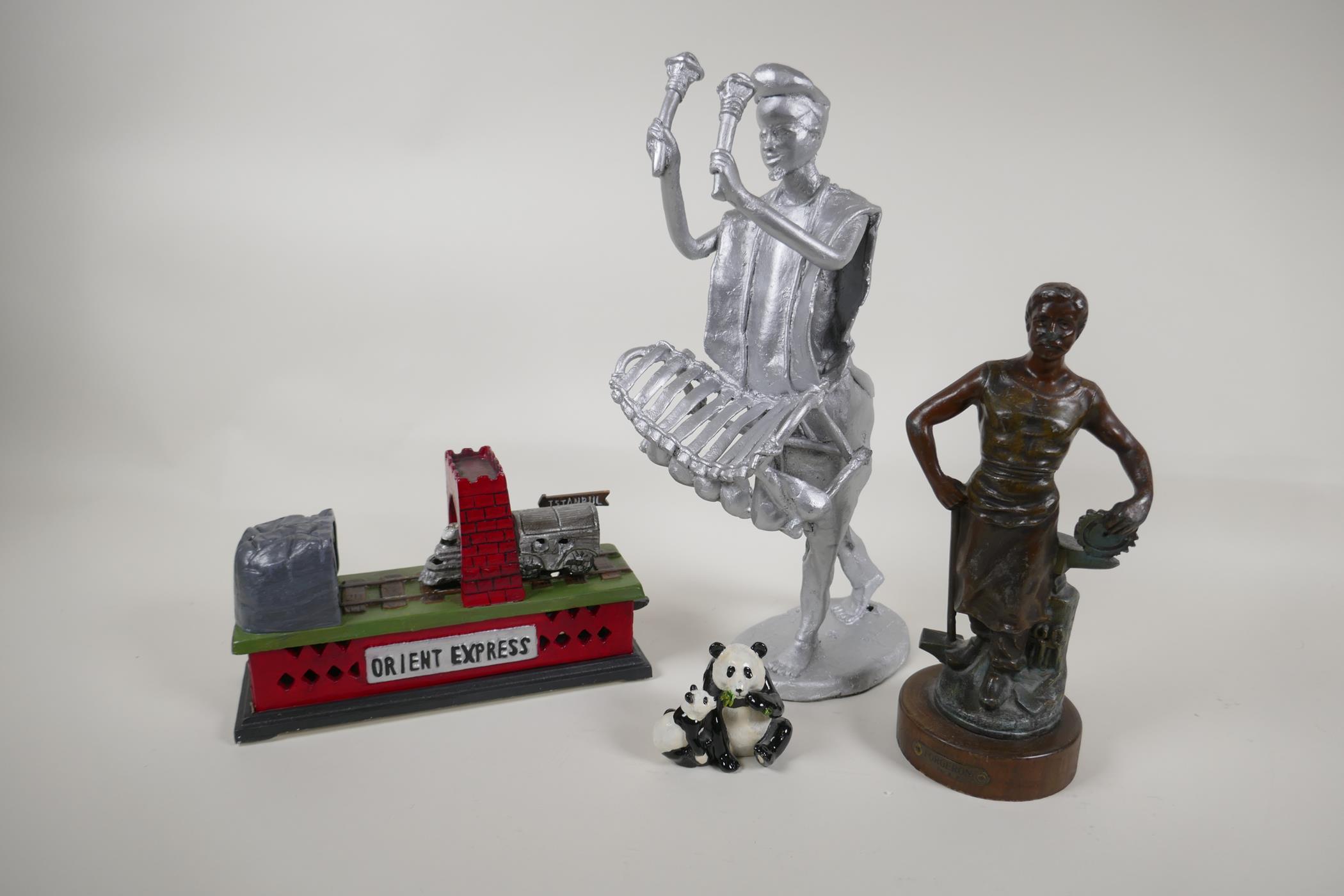 A bronzed spelter figure of a foundry worker, and iron trick train money box, a painted metal figure