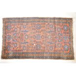 An antique, hand woven wool carpet, with blue geometric designs and floral motifs, on a terracotta