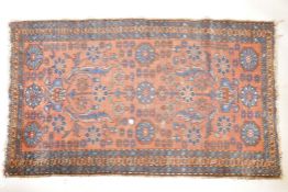 An antique, hand woven wool carpet, with blue geometric designs and floral motifs, on a terracotta