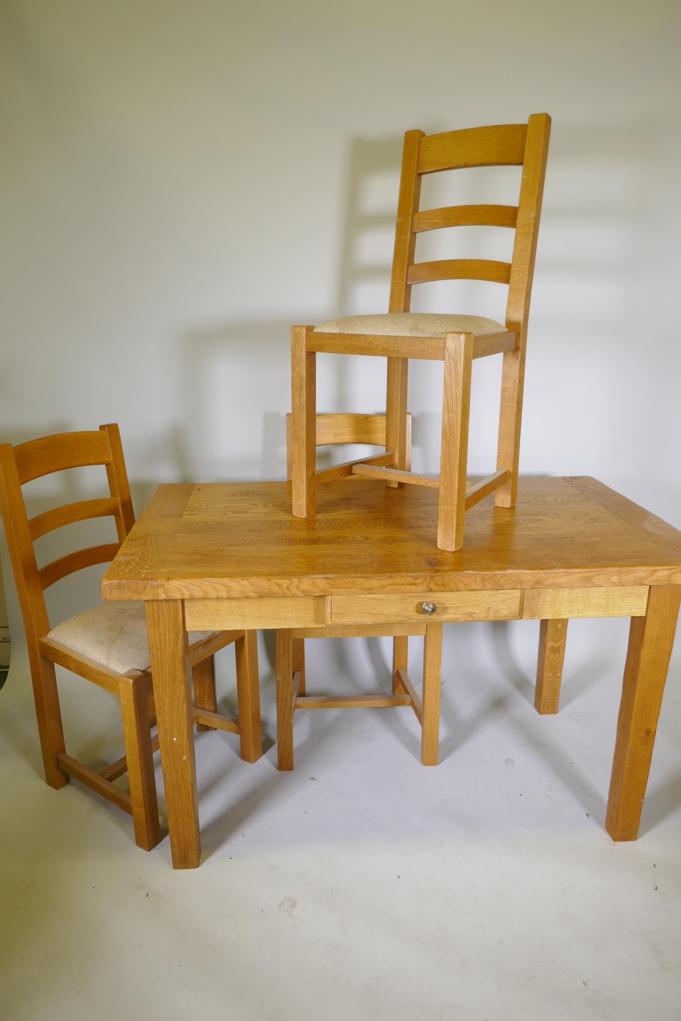 A blond oak kitchen table with single drawer and three matching ladder back dining chairs, 51½" x