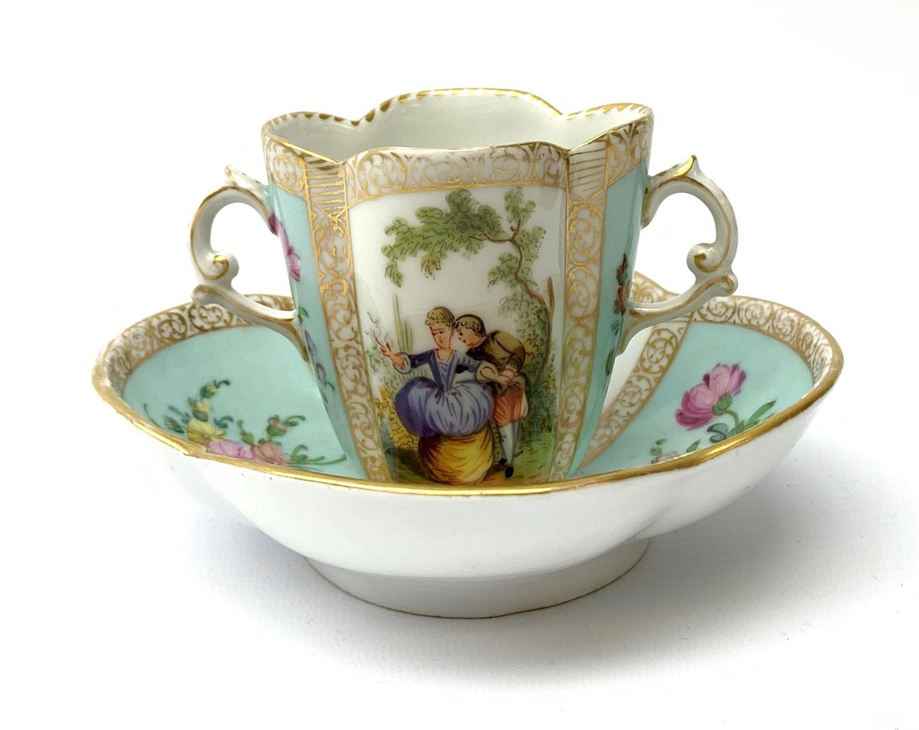 A Helena Wolfsohn Dresden porcelain quatrefoil twin handled chocolate cup and stand, painted with pa