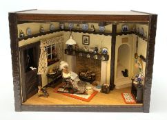 A 1/12th scale diorama of a cottage sitting room, depicting an elderly lady seated before a fireplac
