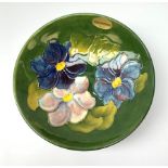 A Moorcroft footed dish decorated in the anemone pattern upon a green glazed ground