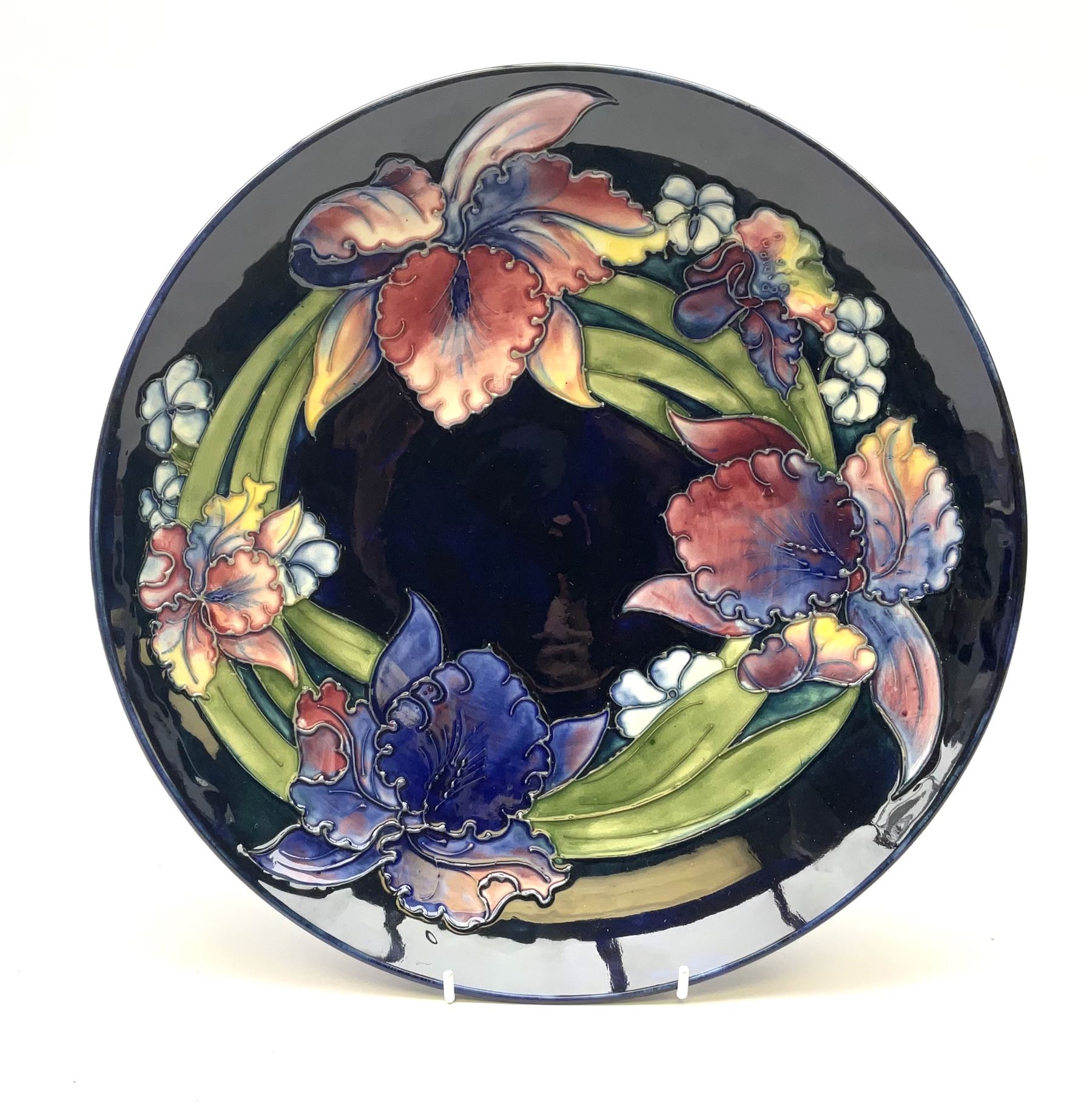A Moorcroft footed dish decorated in the iris pattern upon a dark blue glazed ground