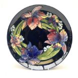 A Moorcroft footed dish decorated in the iris pattern upon a dark blue glazed ground