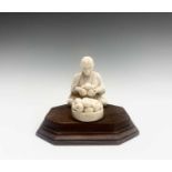 An Indian ivory model of a seated fruit vendor, early 20th century, on an octagonal hardwood base,