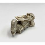 A Japanese ivory netsuke, early 20th century, modelled as a recumbent male smoking a pipe, height