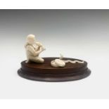 An Indian ivory model of a snake charmer, early 20th century, seated on an oval wooden base,
