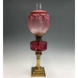 A late Victorian cranberry glass and brass oil lamp, raised on Corinthian column base and with