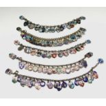 Five chain bracelets each filled with a mass of enamelled charms, nearly all are silver and many
