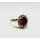 A gold ring with an oval red stone and diamond cluster 5.3gm